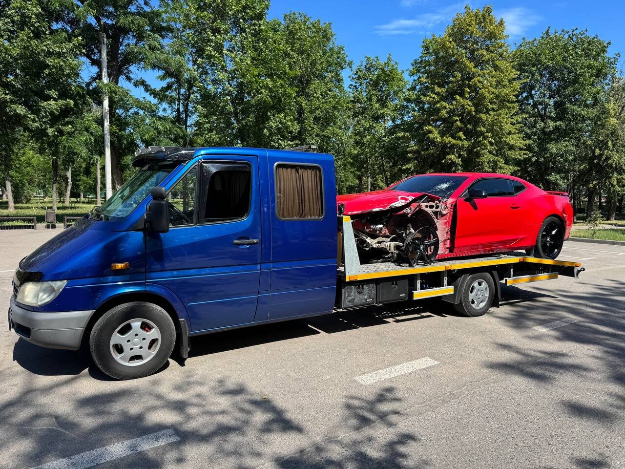 Синій евакуатор перевозить червоне пошкоджене купе